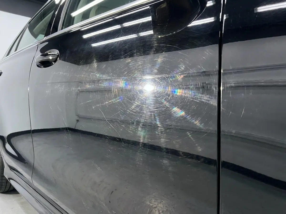 Black car panel with swirl marks before paint correction